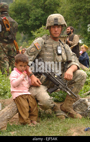 A little boy sits and holds the hand of U.S. Army Sgt. Resolve Savage, from Charlie Company, 1st Battalion, 158th Infantry Regiment, Arizona National Guard, while he pulls security outside of a hospital during a medical capabilities program and humanitarian assistance supply hand out in the Nuristan province of Afghanistan June 28, 2007.  Staff Sgt. Isaac A. Graham Stock Photo