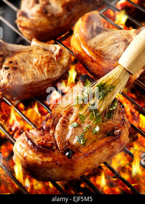 Cooking on a BBQ with hot coals and lamb cutlets being marinated with rosemary Stock Photo