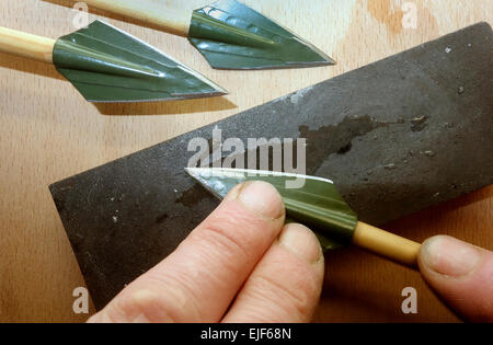 Broadhead arrowhead on wooden shaft are in process of sharpening for big game hunt purpose. Stock Photo