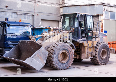 Front end loader with its bucket or scoop down parked in front of a warehouse on paving Stock Photo