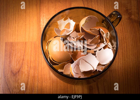 A glass cup of smashed crushed and broken eggshells on natural wood background Stock Photo