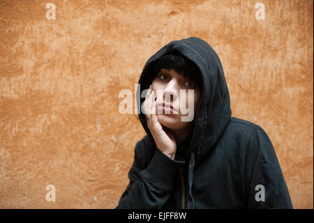 Dark young sad woman posing looking at camera near orange urban wall Stock Photo
