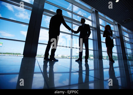 Male office workers standing by the window and handshaking with their colleague near by Stock Photo