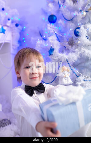 little boy in a white shirt and bow tie decorates a Christmas tree Stock Photo