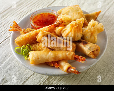 Cooked mixed Chinese starters - Dim sum, breaded prawns, spring rolls with chilli sauce served on a white plate