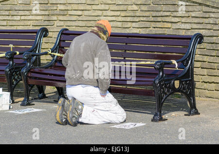 Workman kneeling down painting a wooden bench. Stock Photo