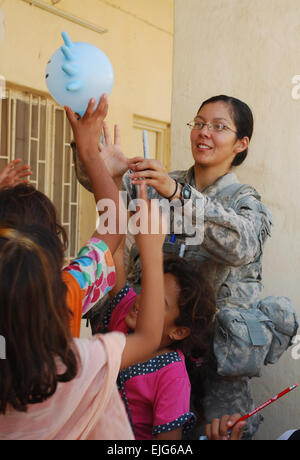 Spc. Jessica Velasquez, of Gardena, Calif., makes a balloon animal out of a surgical glove and hands it off to a group of excited Iraqi girls at an elementary school during a recent combined humanitarian assistance mission in the town of Salman Pak, Iraq, located 30 miles southeast of Baghdad. Velasquez was one of six U.S. medics on hand to assist Iraqi medical personnel during the recent mission. Velasquez serves as a medic assigned to Company C, 82nd Brigade Support Battalion, 3rd Brigade Combat Team, 82nd Airborne Division, Multi-National Division-Baghdad, and is currently serving in her fi Stock Photo