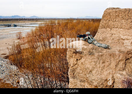 Spc. Jeremy Burton, armored crewman, assigned to 2nd Squad, 3rd Platoon, Company C., 1st Battalion, 66th Armored Regiment, 1st Brigade Combat Team, 4th Infantry Division, lays in the prone position on cliff overlooking the Arghandab River Valley Jan. 31, to provide security for his squad as they climb up the cliff from the valley below. Burton, a native of Birmingham, Ala., was conducting a foot patrol with his squad to search orchards throughout the district and interact with the local population. During their foot patrols, 2nd squad must maneuver their way through the Arghandab‘s many obstac Stock Photo