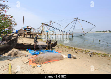 Local fishermen tending their nets on the beach and traditional Chinese fishing nets at Fort Cochin, Kerala, southern India Stock Photo