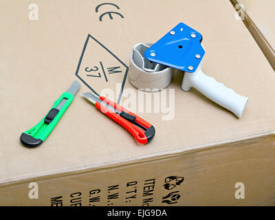 Packaging Tape Gun Dispenser and stationary knives lying on cardboard box Stock Photo