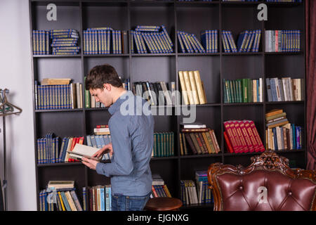 Serious Young Young Man Scanning a Book While Standing In Front of the Shelves at the Library Stock Photo