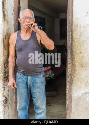 Hispanic Cuban man stands in the doorway of his home smoking cigar Stock Photo