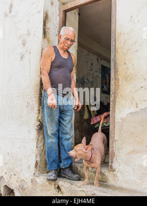 A Hispanic Cuban man stands in the doorway of his house in Havana Vieja, Cuba with dog beside him. Stock Photo