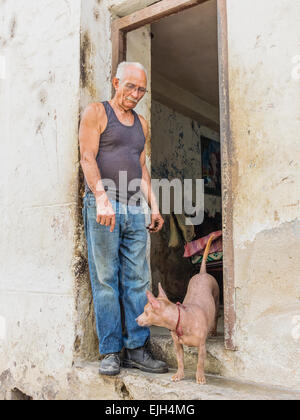 A Hispanic Cuban man stands in the doorway of his house in Havana Vieja, Cuba with dog beside him. Stock Photo