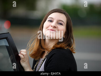 Young woman with long hair posing in the street, looking at the camera and smiling. Shallow depth of field. Focus on the model's Stock Photo