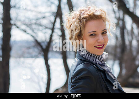 Portrait of a pretty young woman with blond curly hair smiling and going away in the woods by the river Stock Photo