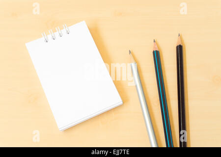 Three Pencils with White Notebook on Light Brown Wooden Table Stock Photo