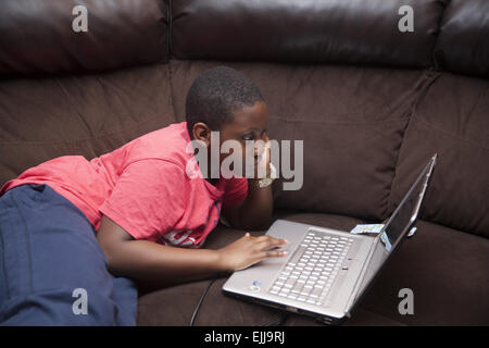 Adolescent boy does school research on a computer on the couch at home in Brooklyn, NY. Stock Photo