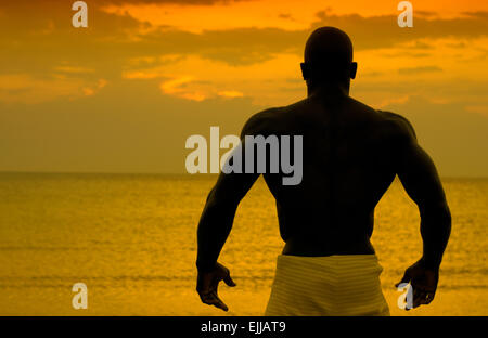 Silhouette of bodybuilder posing at the sunrise on the beach, training in the morning, strong man showing his muscles Stock Photo