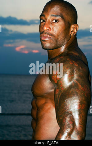 Silhouette of bodybuilder posing at the sunrise on the beach, training in the morning, strong man showing his muscles Stock Photo
