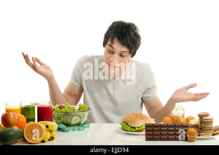 Man choosing between fruits, smoothie and organic healthy food against sweets, sugar, lots of candies and a big hamburger, fast  Stock Photo