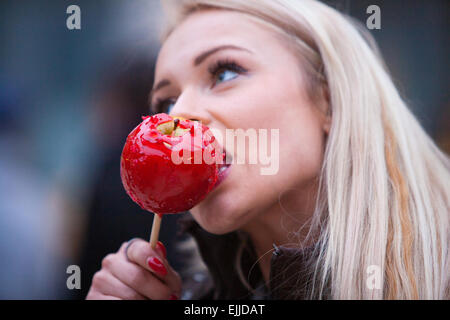 blonde woman tasting a red apple candy in an European city Stock Photo