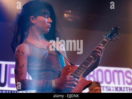 Male lead guitarist of a rock band with long black hair and tattoos on stage at a concert. Stock Photo