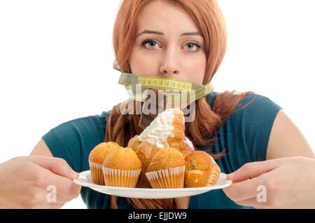 Woman with a centimeter on her mouth unable to eat all the sweets and sugar, lots of cookies on a plate. Dieting without sweets Stock Photo
