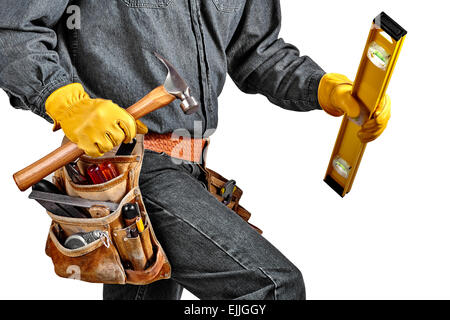 Man in black denim wearing used tool belt filled with carpenter tools carrying a yellow level, hardhat and hammer Stock Photo