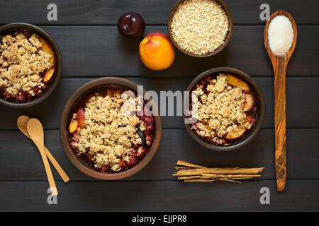 Overhead shot of rustic bowls filled with baked plum and nectarine crumble or crisp, photographed on dark wood Stock Photo