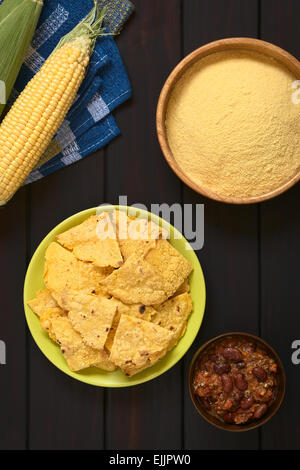 Overhead shot of homemade baked corn chips on plate with cornmeal, corn cobs and a small bowl of chili con carne Stock Photo