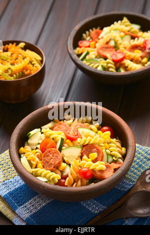 Two rustic bowls of pasta salad made of tricolor fusilli, sweet corn, cucumber, cherry tomato and sausage Stock Photo