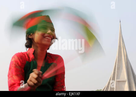 A Bangladeshi child holds a national flag as she stands in front the National Monument for the Martyrs of the Liberation War of Bangladesh in Savar Stock Photo