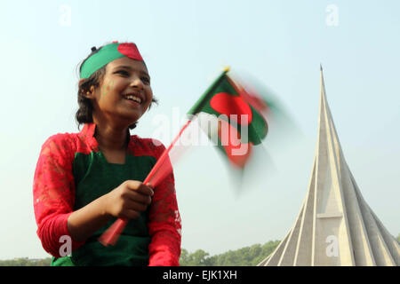 A Bangladeshi child holds a national flag as she stands in front the National Monument for the Martyrs of the Liberation War of Bangladesh in Savar Stock Photo