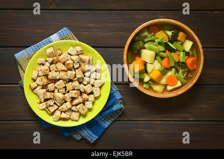 Overhead shot of homemade croutons and bowl of vegetable soup made of zucchini, green bean, carrot, potato, pumpkin, broccoli Stock Photo