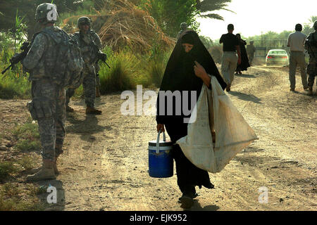 An Iraqi woman walks between Soldiers as they pull security for a mission outside Scania Base, Iraq, Aug, 19, 2009. The mission was to check on the condition of a water treatment facility, which filters water for six nearby villages. The Soldiers are assigned to Company A, 2nd Battalion, 162nd Infantry Regiment, 41st Infantry Brigade Combat Team, Oregon Army National Guard.    Spc. Anita VanderMolen. Stock Photo