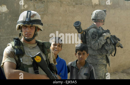 An Iraqi army soldier is flanked by two boys as a U.S. Army Soldier assigned to Alpha Battery provides security during a joint mission in Khan Bani Sa'ad, Iraq, July 12, 2007.  Soldiers from Alpha Battery, 2nd Battalion, 12th Field Artillery Regiment, 4th Stryker Brigade Combat Team, 2nd Infantry Division and units of the Iraqi army are conducting a cordon and search mission to clear the area of insurgents and cache sites.  Mass Communication Specialist 2nd Class Scott Taylor Stock Photo