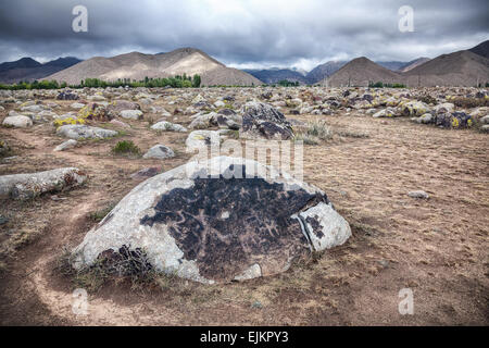 Ancient petroglyph with hunter and animals on the stone in open air museum of Kyrgyzstan at overcast mountain background Stock Photo