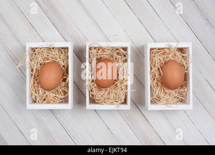 Three brown eggs in wood crates on a whitewashed wood surface. High angle shot in horizontal format. Stock Photo