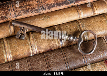 Large rusty key lying on weathered old books Stock Photo