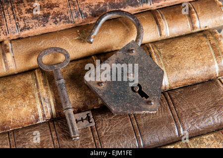 Open padlock and rusty key lying on ancient books Stock Photo