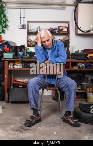 Portrait of frustrated senior worker sitting on the chair in his workshop. Stock Photo
