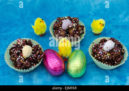 Looking down on a perfect Easter collection of Easter eggs, chocolate cornflake cakes and little baby yellow toy chicks Stock Photo