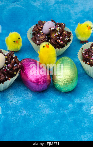 Select view of an image for Easter that includes Easter eggs, chocolate cornflake cakes and little baby yellow toy chicks. Stock Photo