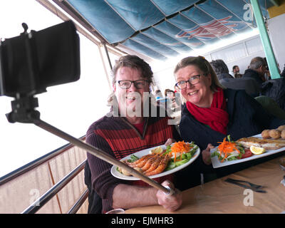 SELFIE  RESTAURANT SMARTPHONE Attractive couple using a "selfie stick" and smartphone to capture image enjoying a meal together in terrace restaurant Stock Photo