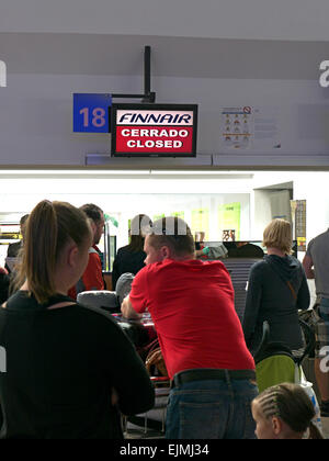 Queue of frustrated airline passengers and luggage wait on airport concourse at closed check in Stock Photo