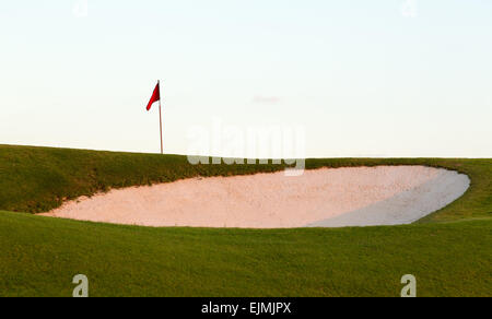 Red flag of golf hole above sand trap or bunker on beautiful course at sunset Stock Photo