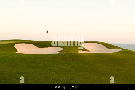 Red flag of golf hole above sand trap or bunker on beautiful ocean front course at sunset Stock Photo