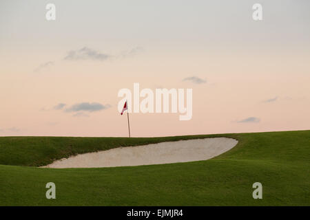 Red flag of golf hole above sand trap or bunker on beautiful course at sunset Stock Photo