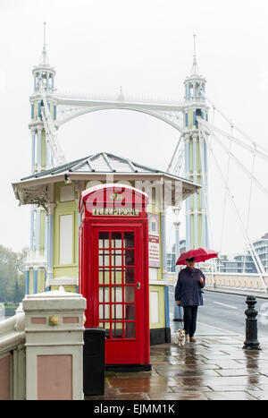 Albert Bridge, red phone booth, pedestrian with umbrella, London Stock Photo